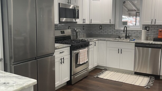Een moderne keuken met roestvrijstalen apparatuur, witte kasten en een backsplash van baksteen.