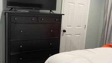 A bedroom with a black dresser, a television on top, a white door, and a bed with white bedding.