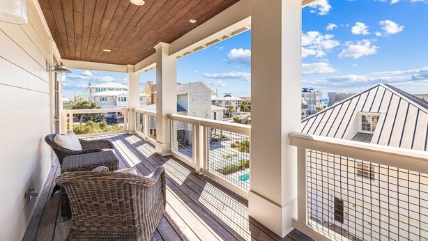 En overdækket balkon med fletmøbler, træloft og udsigt til omkringliggende bygninger.