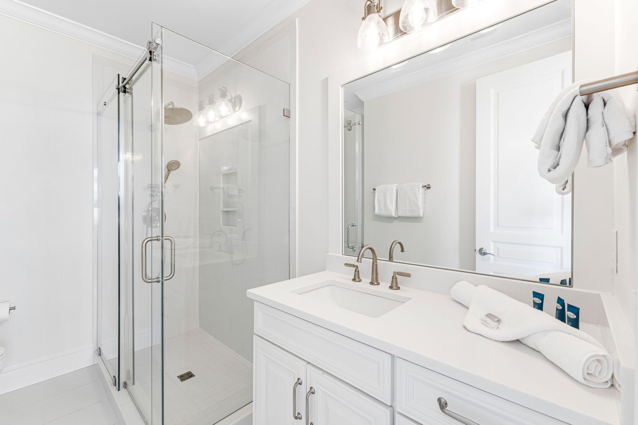 A modern bathroom with a glass-enclosed shower, a large mirror, and a white vanity with drawers and a sink.