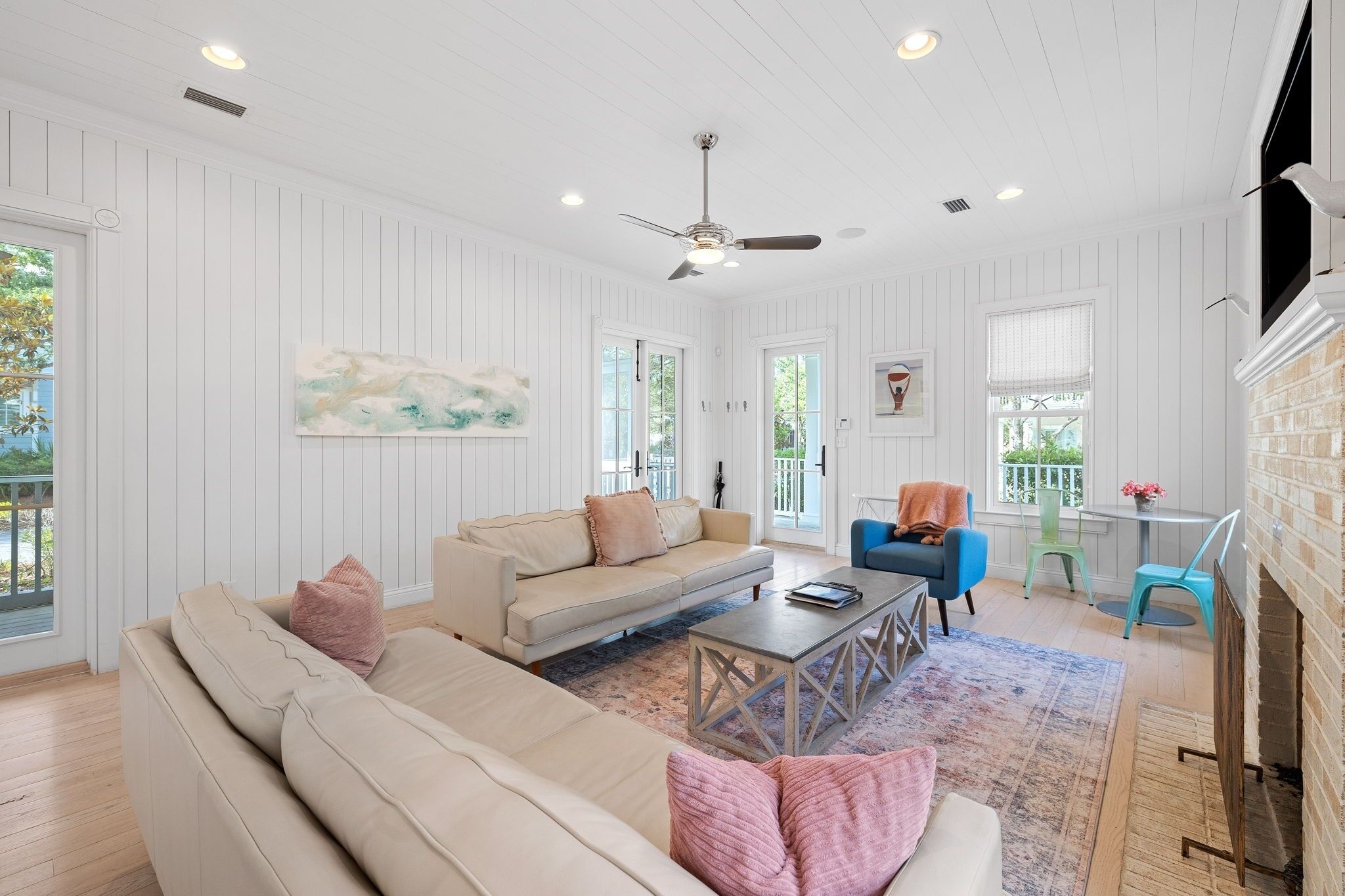 A spacious living room with a beige sofa, a blue armchair, and a coffee table. There is a fireplace on the right and a ceiling fan.
