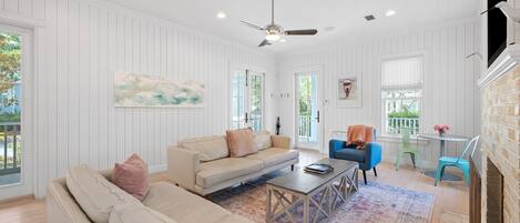 A spacious living room with a beige sofa, a blue armchair, and a coffee table. There is a fireplace on the right and a ceiling fan.