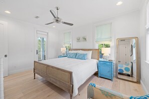 Un dormitorio con una cama de madera, un ventilador de techo, una mesita de noche con lámpara, un aparador y un espejo.