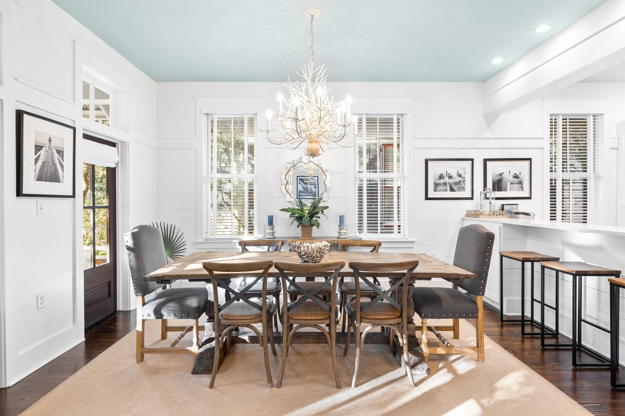 A dining area with a round table, six chairs, a chandelier, and a potted plant.