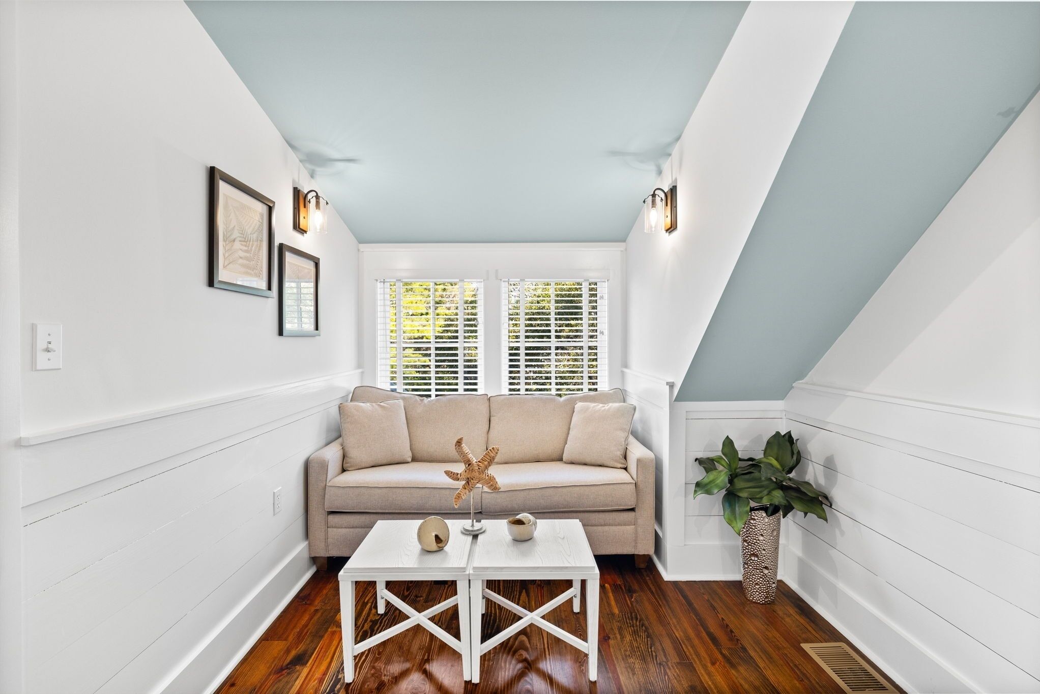 A room with a beige sofa, white crossback chairs, a small white table with decorative items, and a potted plant.