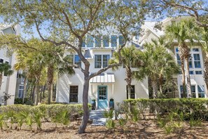 A multi-story building with a central entrance, surrounded by palm trees and well-maintained landscaping. - South Of 30a Close To The Beach + Watercolor Beach Club Evergreen Dream 5 Bedroom Home by RedAwning (Santa Rosa Beach)