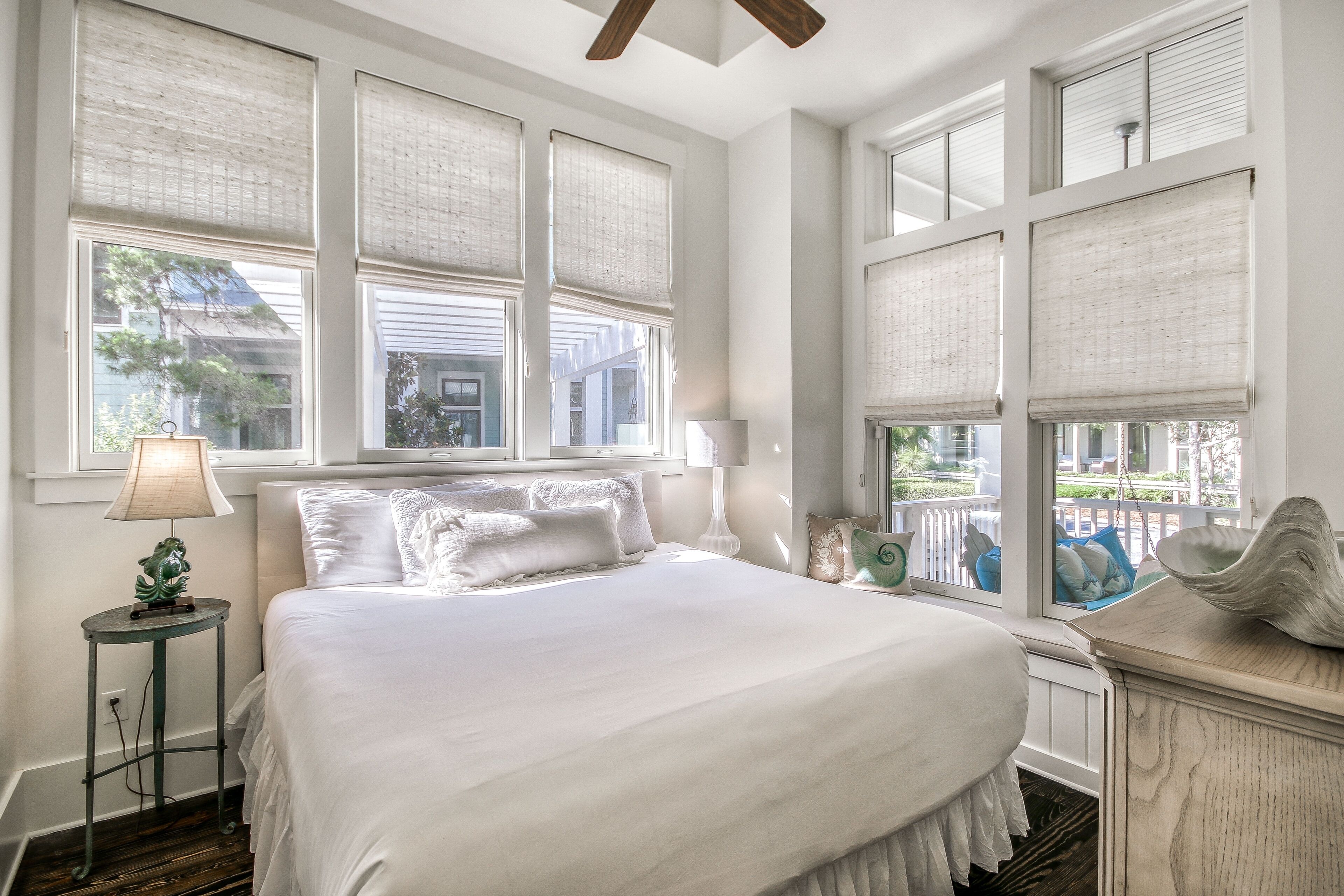 Une chambre avec un grand lit, du linge de lit blanc, une table de chevet avec une lampe, et une vue sur l’extérieur grâce à de nombreuses fenêtres.
