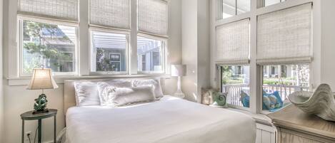 Une chambre avec un grand lit, du linge de lit blanc, une table de chevet avec une lampe, et une vue sur l’extérieur grâce à de nombreuses fenêtres.