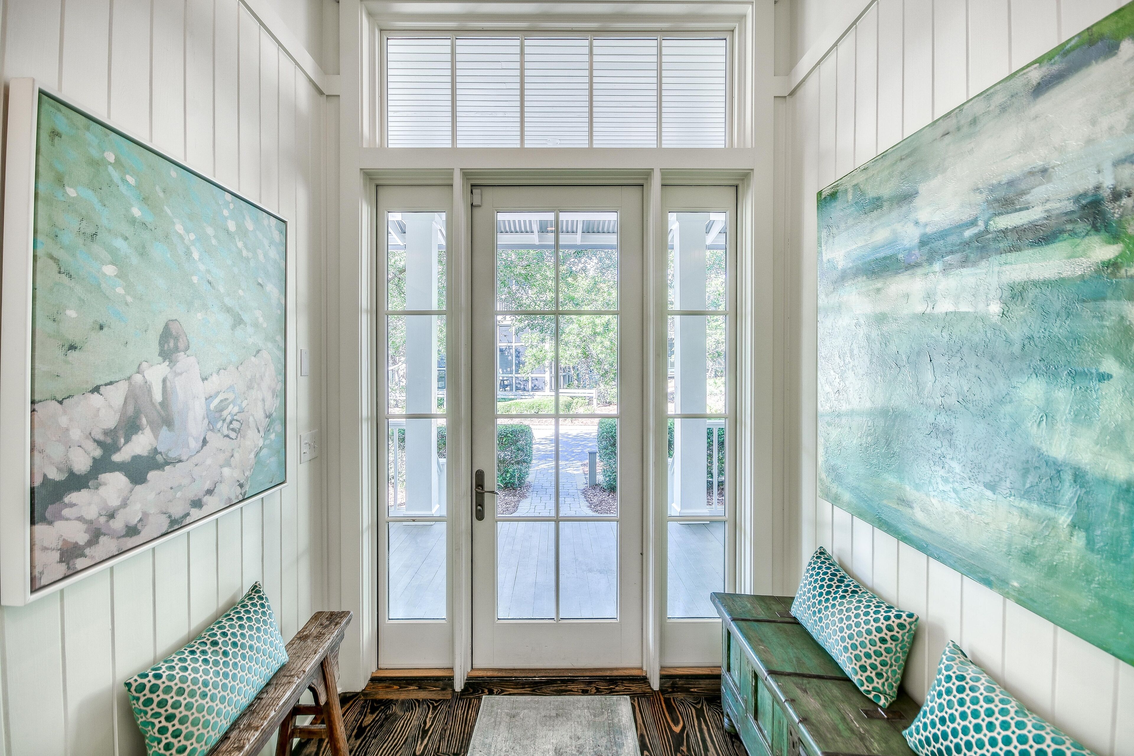 A room with a large window, a bench, and a painting on the wall.