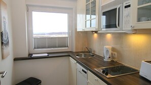 A compact kitchen with a window, a microwave, a toaster, and a sink. - TOP vacation apartment for up to 2 people. Bright and modern furnishings. (Hörnum)