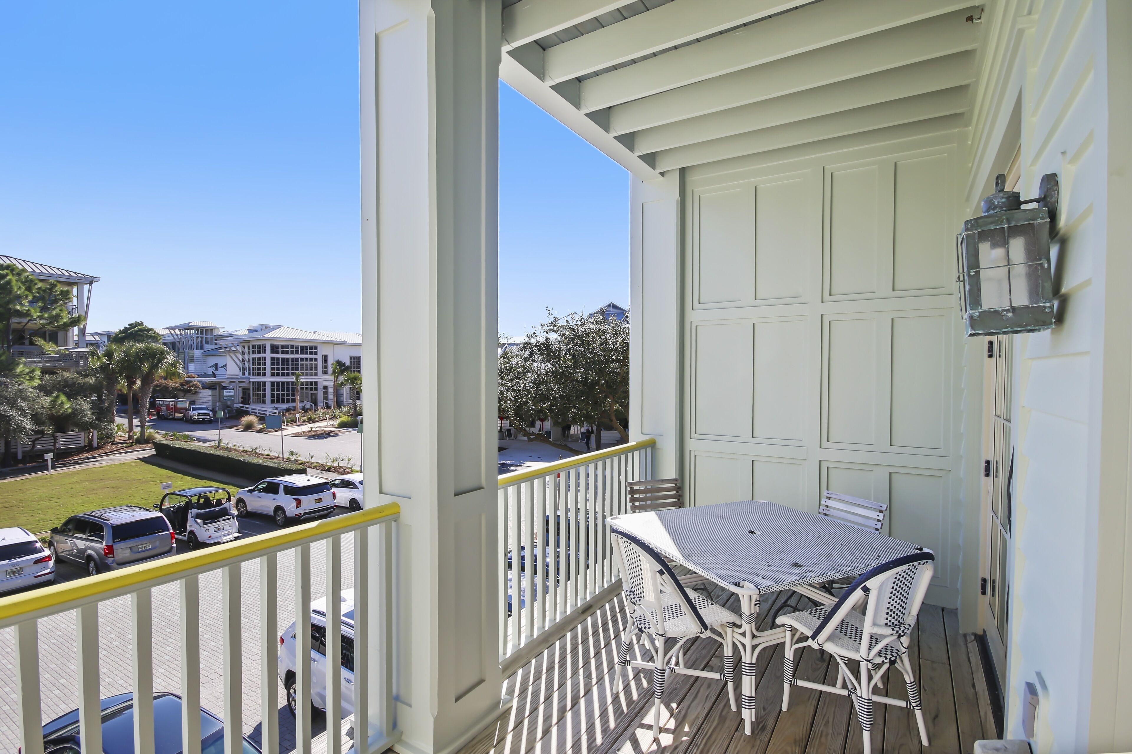 A balcony with a table and chairs, a view of parked cars, and a building in the background.