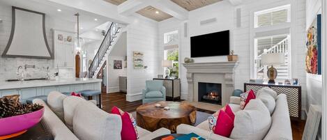 A spacious living room with a fireplace, a television mounted on the wall, and a staircase leading to another level.