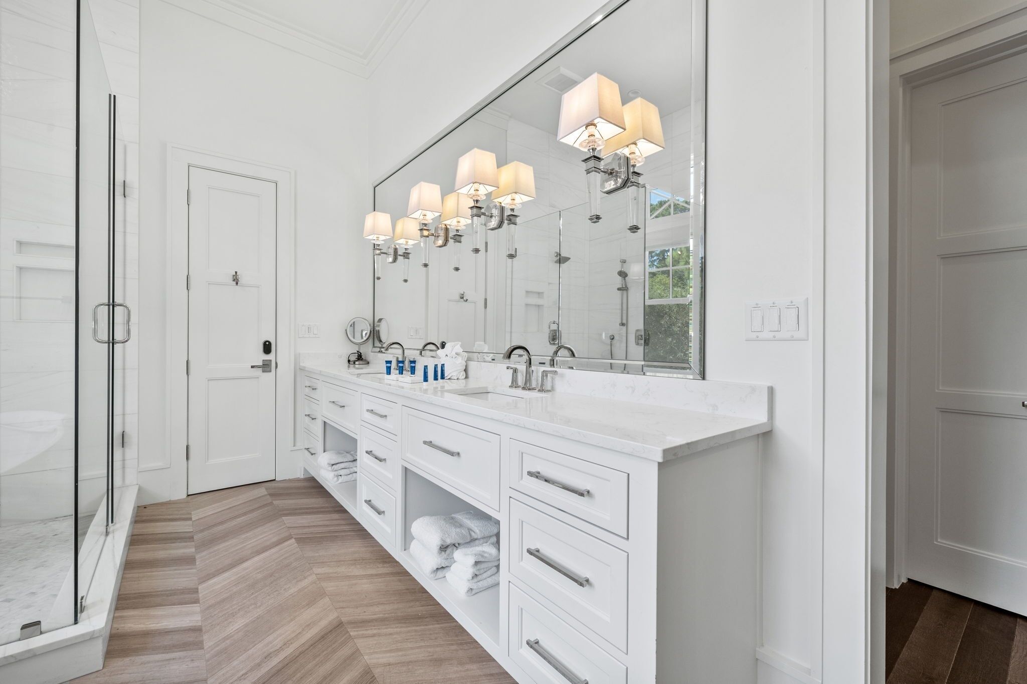 Un baño moderno con un espejo grande, muebles blancos y una zona de ducha.