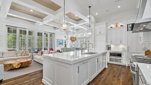 A spacious kitchen with white cabinetry, a large island, and a dining area with a wooden coffee table. - "Stress Free" Golf Cart Pool Exquisite, 6 bedroom, new construction home WaterColor 6 Home by RedAwning (Santa Rosa Beach)