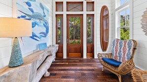 A wooden floor, a bench, a chair, a wall with a painting, and a door with glass panels. - "Stress Free" Golf Cart Pool Exquisite, 6 bedroom, new construction home WaterColor 6 Home by RedAwning (Santa Rosa Beach)
