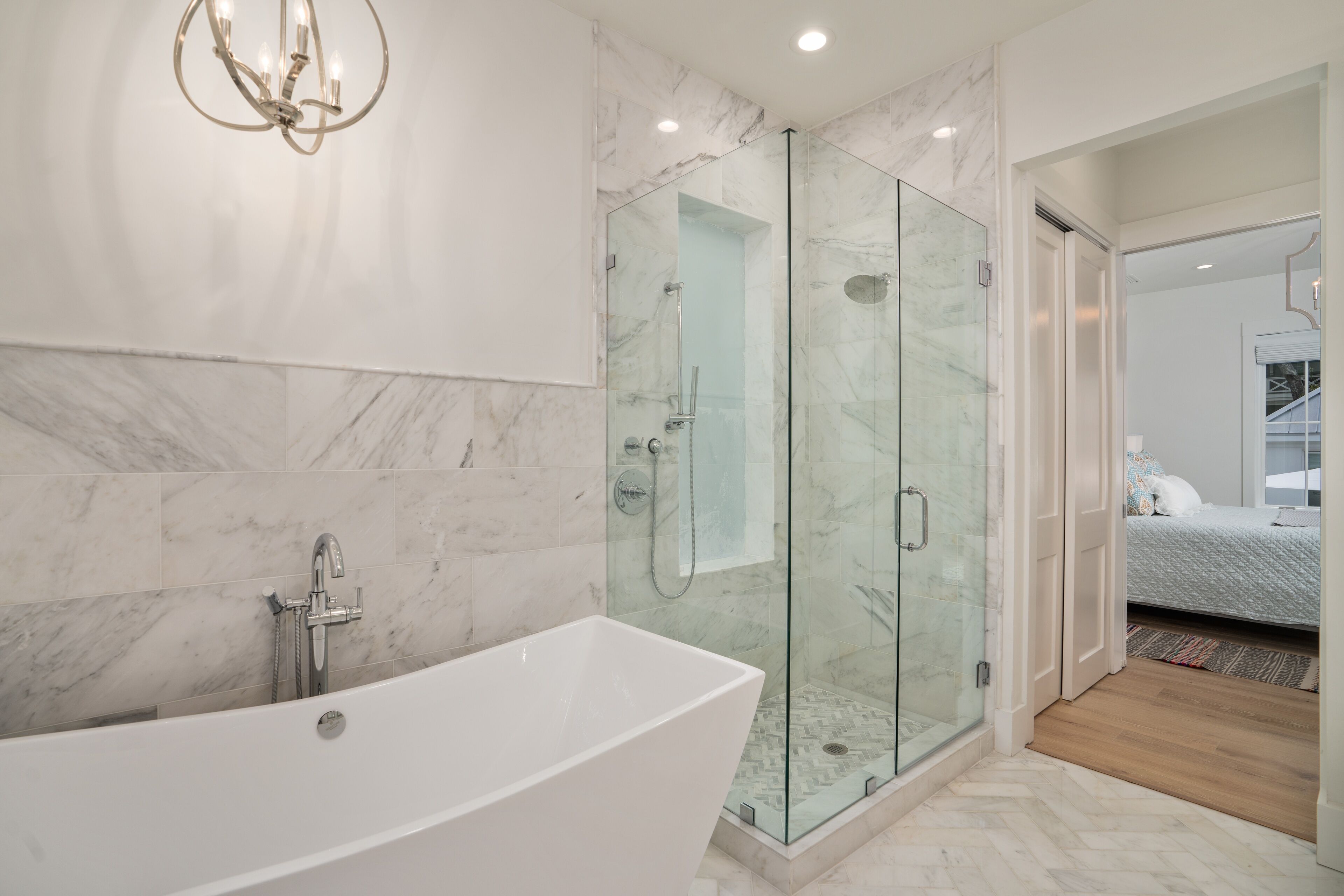A modern bathroom with a freestanding bathtub, a glass-enclosed shower, and a marble-tiled wall.