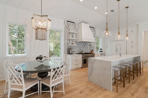 A modern kitchen with a large island, white cabinetry, and a dining area with white chairs. - Upscale Beach Estate With Private Pool + Carriage House And Less Than 300 Yards From The Beach 6 Bedroom Home by RedAwning (Santa Rosa Beach)