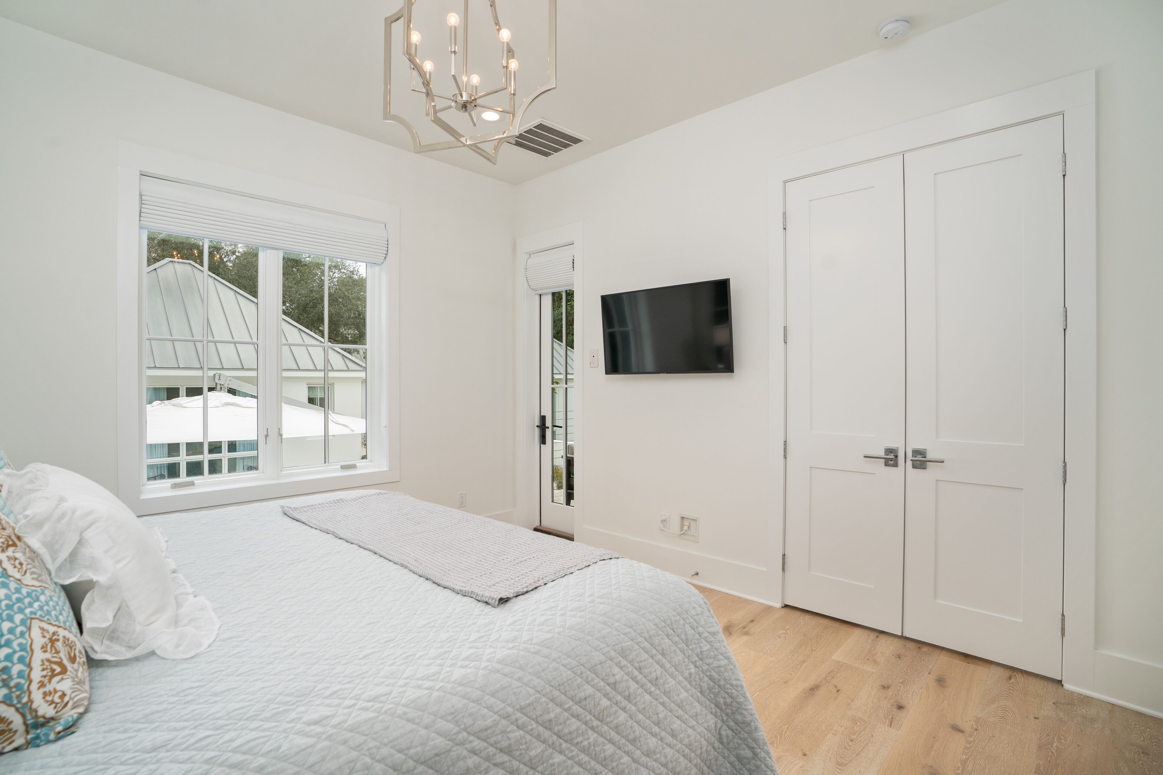 A bedroom with a large bed, a TV mounted on the wall, and a window with a view of a greenhouse.