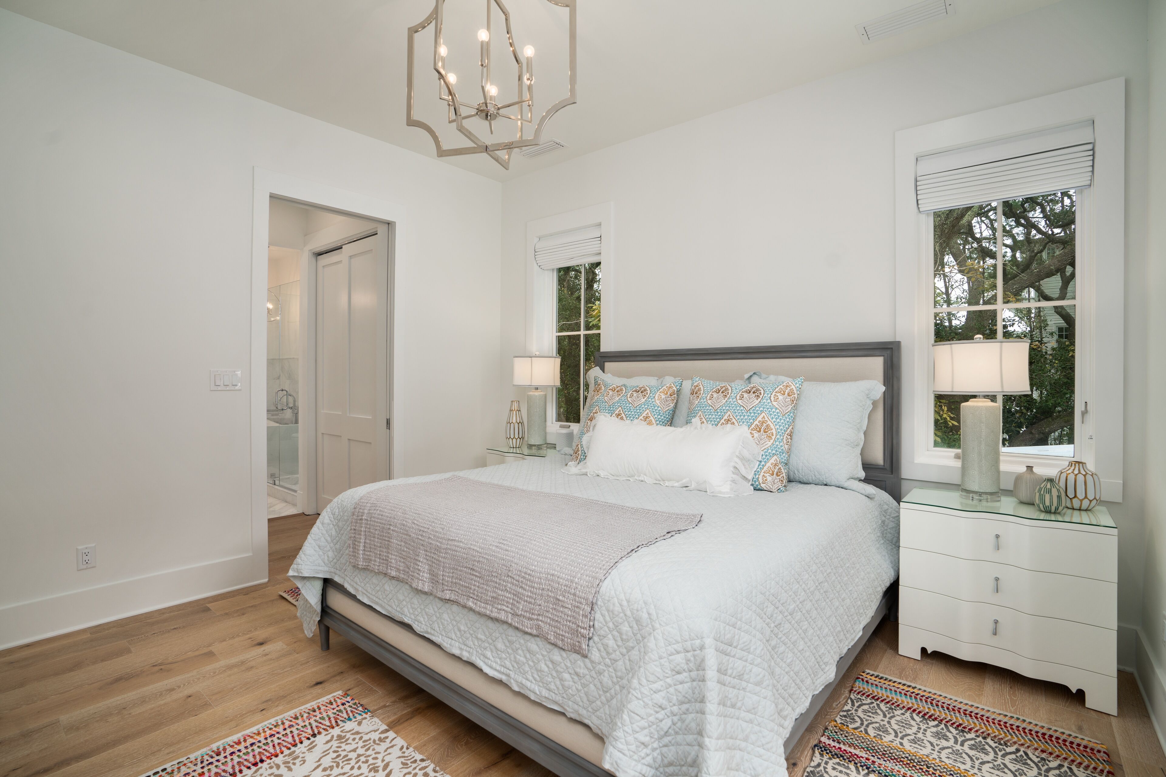 Une chambre à coucher avec un lit, des tables de chevet, un lustre et une fenêtre avec des stores.