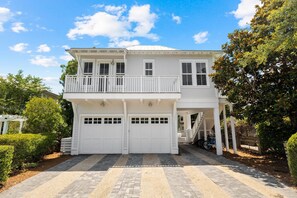 Una casa a due piani con un balcone, due porte per garage e un portico coperto.