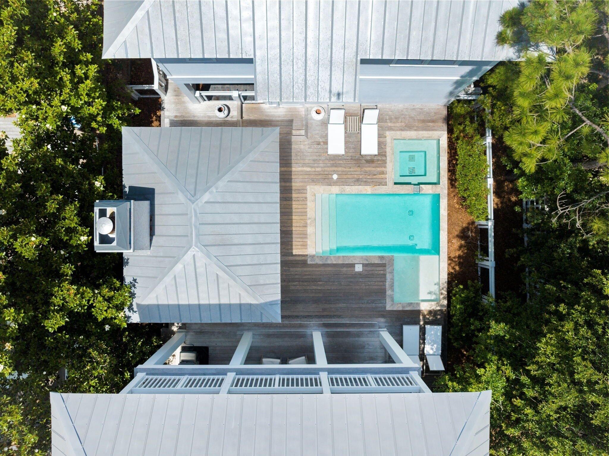 An aerial view of a house with a swimming pool, wooden deck, and a covered outdoor seating area.