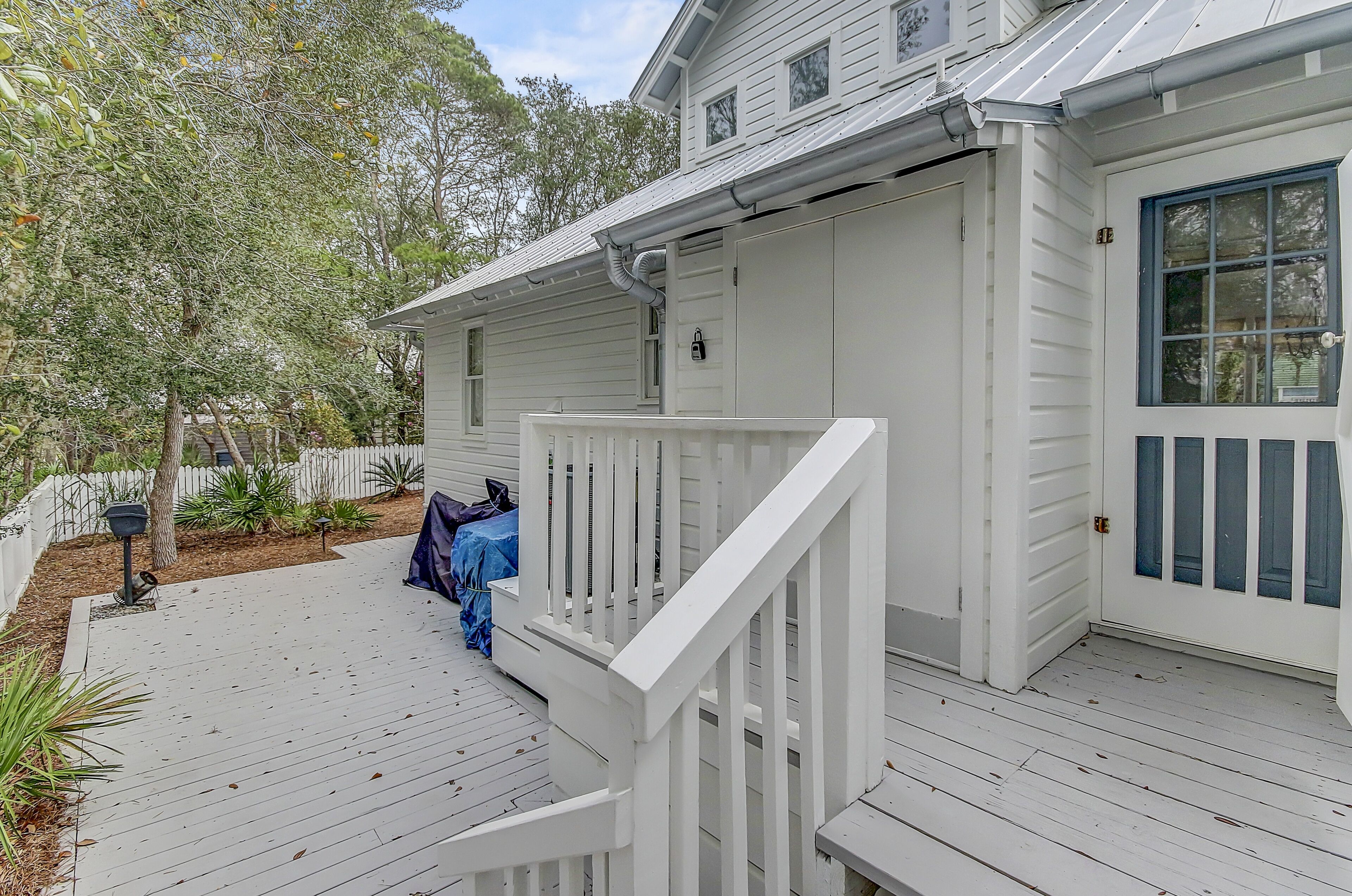 A white house with a porch, a covered area, and a fenced yard.