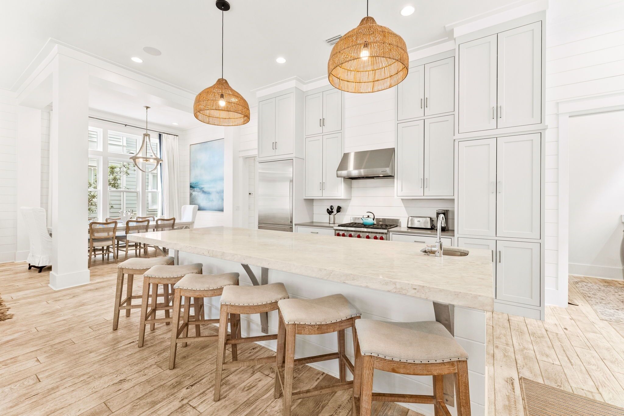 A spacious kitchen with white cabinetry, a large island with bar stools, and hanging wicker pendant lights.