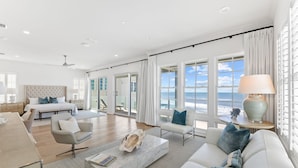 A spacious living room with a large bed, a sofa, and a coffee table. There are large windows with ocean views.