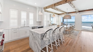 A modern kitchen with white cabinetry, a marble island, and a dining area with white chairs.