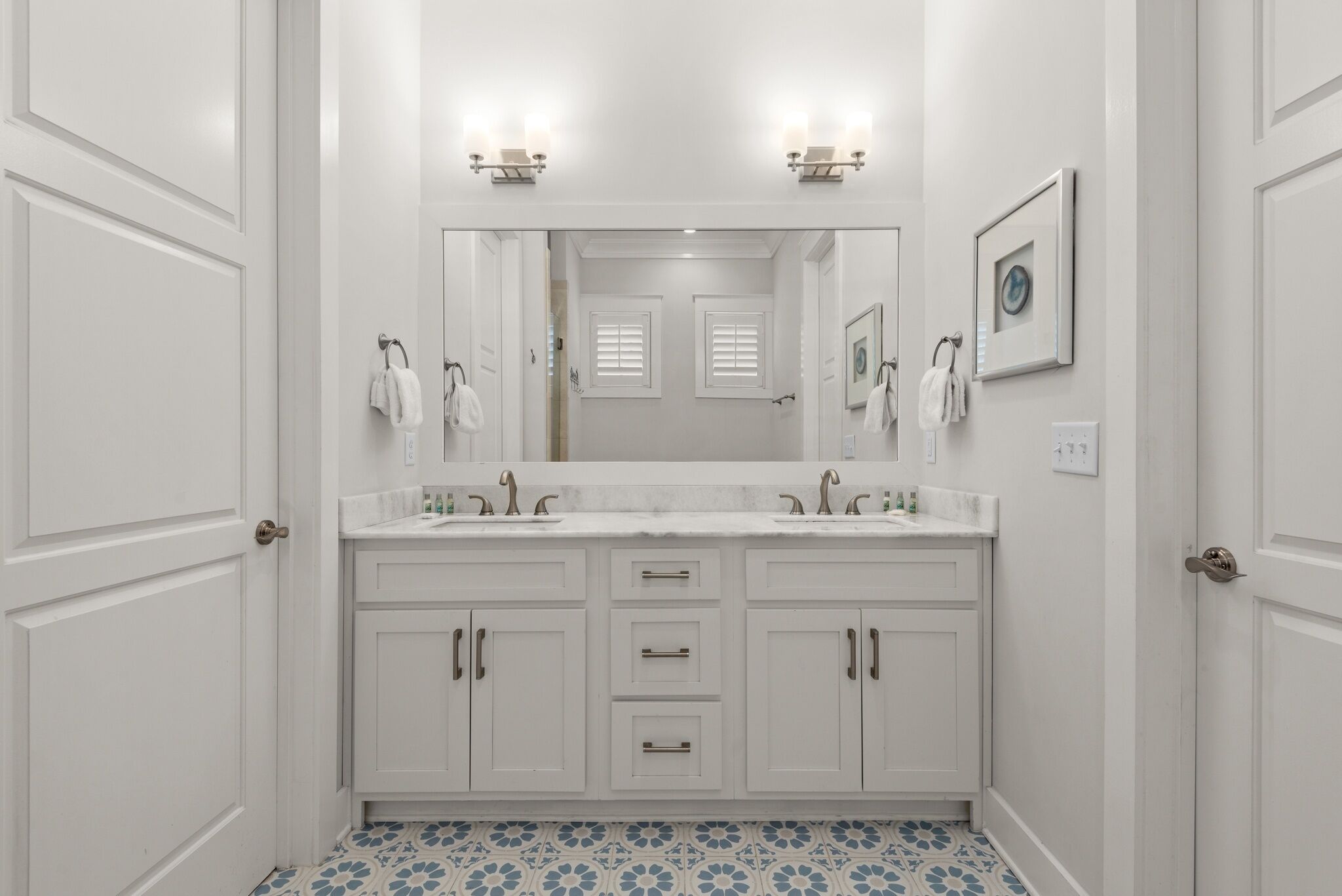 A bathroom with white cabinetry, a double sink vanity, and a large mirror.