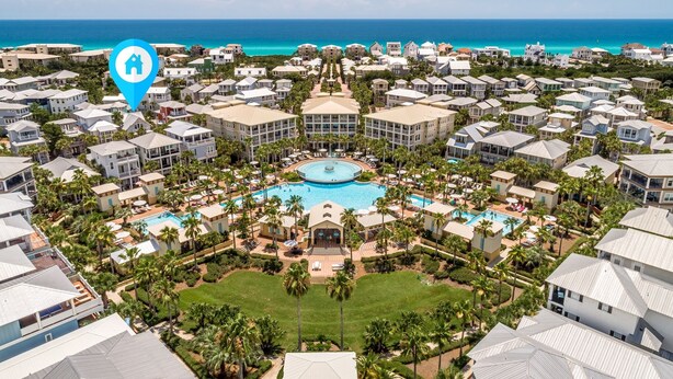 A resort with multiple buildings, a central pool, and a view of the ocean.