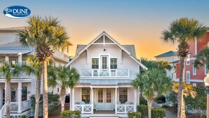A two-story house with a balcony, surrounded by palm trees and a brick pathway.