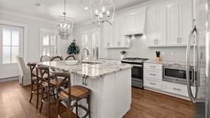 A modern kitchen with white cabinets, a large island with bar stools, stainless steel appliances, and pendant lighting.
