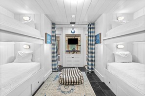 Two single beds with white bedding are positioned on either side of a central area, complemented by a striped ottoman and patterned rug.