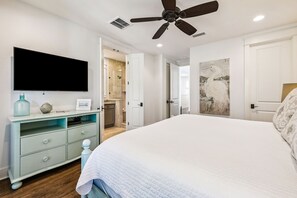 Ein Schlafzimmer mit einem großen Bett, einem Deckenventilator, einem Flachbildfernseher, einer hellblauen Kommode und einem durch eine offene Tür einsehbaren Badezimmer.