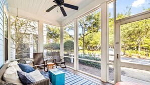 A covered porch with wicker furniture, a ceiling fan, and large windows offering a view of the outdoors. - 'seas The Day' In Watercolor Beach 5 Bdrm/slps 10 Steps To Dragonfly Pool! 5 Bedroom Home by RedAwning (Santa Rosa Beach)