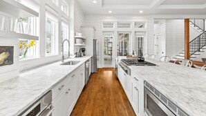 A modern kitchen with white cabinetry, a marble countertop, and a wooden floor. - Pet Friendly Watercolor 4br Home In The Lake District 4 Bedroom Home by RedAwning (Santa Rosa Beach)