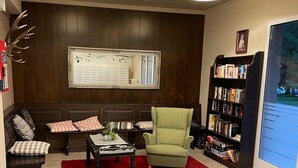 A cozy living room with a sofa, armchair, and coffee table, a bookshelf, and a large mirror on the wall.