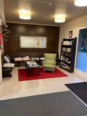 Un salon chaleureux avec un canapé, un fauteuil et une table basse, une bibliothèque et un grand miroir au mur.