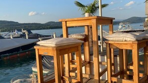 A wooden deck with two bar stools, a table, and an umbrella providing shade.