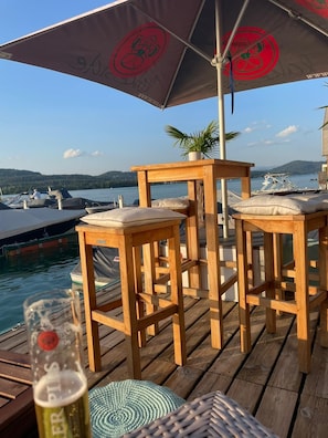Une terrasse en bois avec deux tabourets de bar, une table et un parasol pour faire de l’ombre.