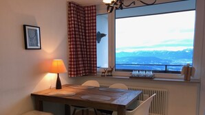 A dining area with a wooden table, white chairs, and a view of mountains through a window.