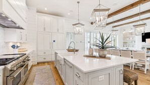 Una cocina amplia con armarios blancos, una isla grande, electrodomésticos de acero inoxidable y luces colgantes.