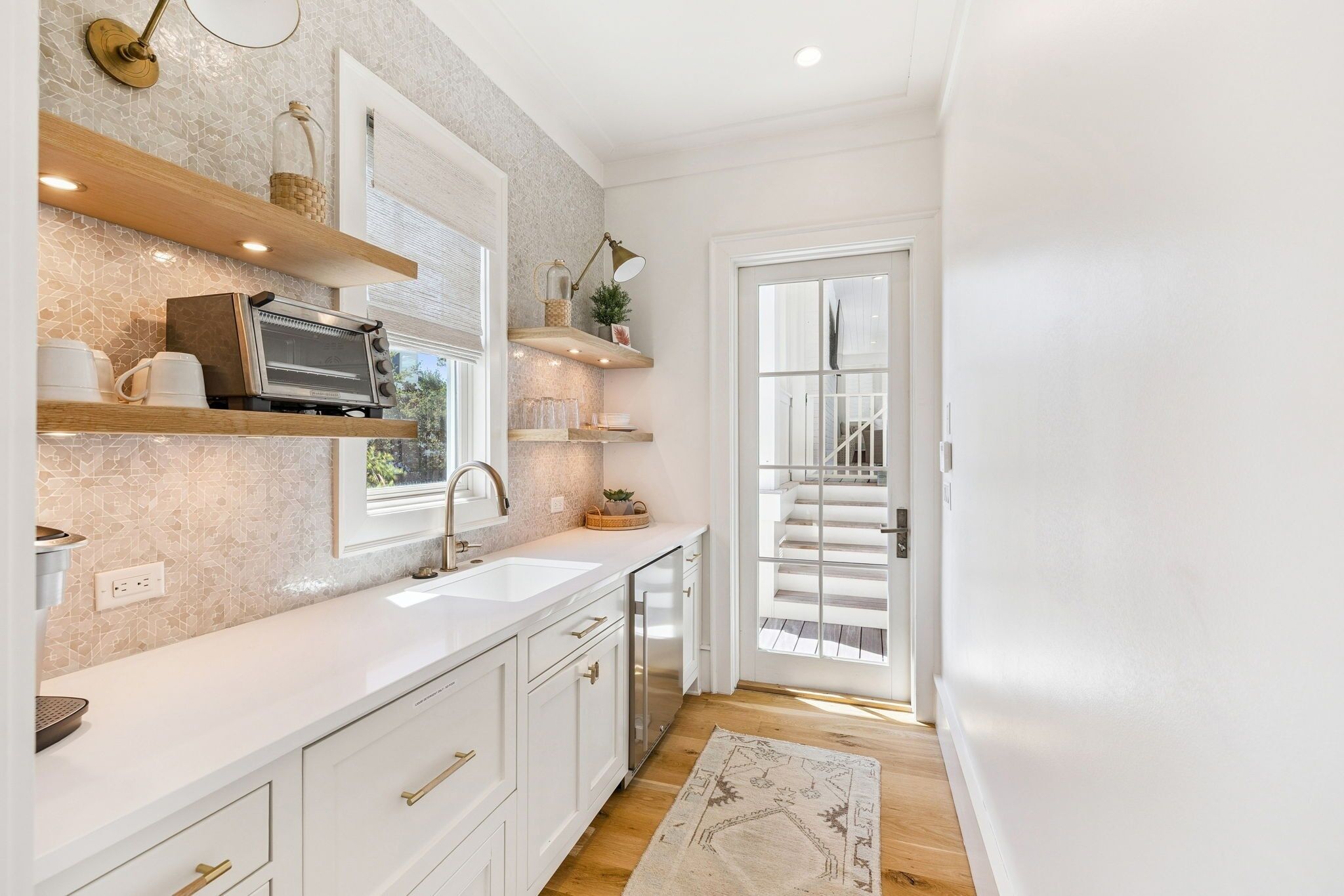 A modern kitchen with white cabinetry, a built-in oven, and a window overlooking a staircase.