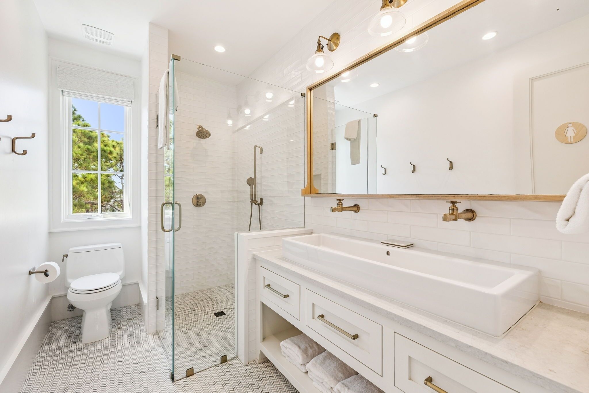 Une salle de bain moderne avec une douche à parois de verre, un grand miroir et un lavabo blanc agrémenté de robinetterie dorée.