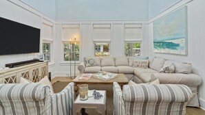 A spacious living room with a large flat-screen TV, a beige sectional sofa, striped armchairs, and a coffee table. - Golf Cart Screened-in Porch & Grill Station Close To Camp Watercolor 4 Bedroom Home by RedAwning (Santa Rosa Beach)