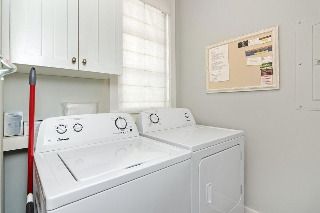 A laundry area with two white Amana washing machines, a red mop, and a bulletin board on the wall.