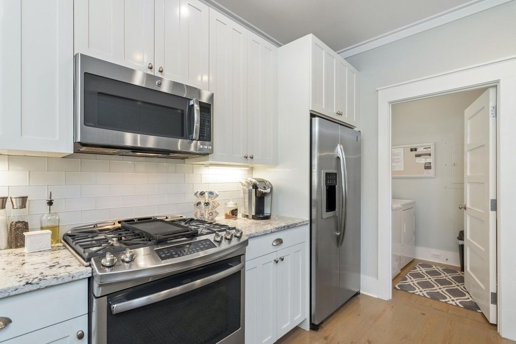 A modern kitchen with white cabinets, stainless steel appliances, and a tiled backsplash.