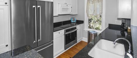 Una cocina moderna con electrodomésticos de acero inoxidable, armarios blancos y una encimera de granito negro, además de una ventana con cortina.