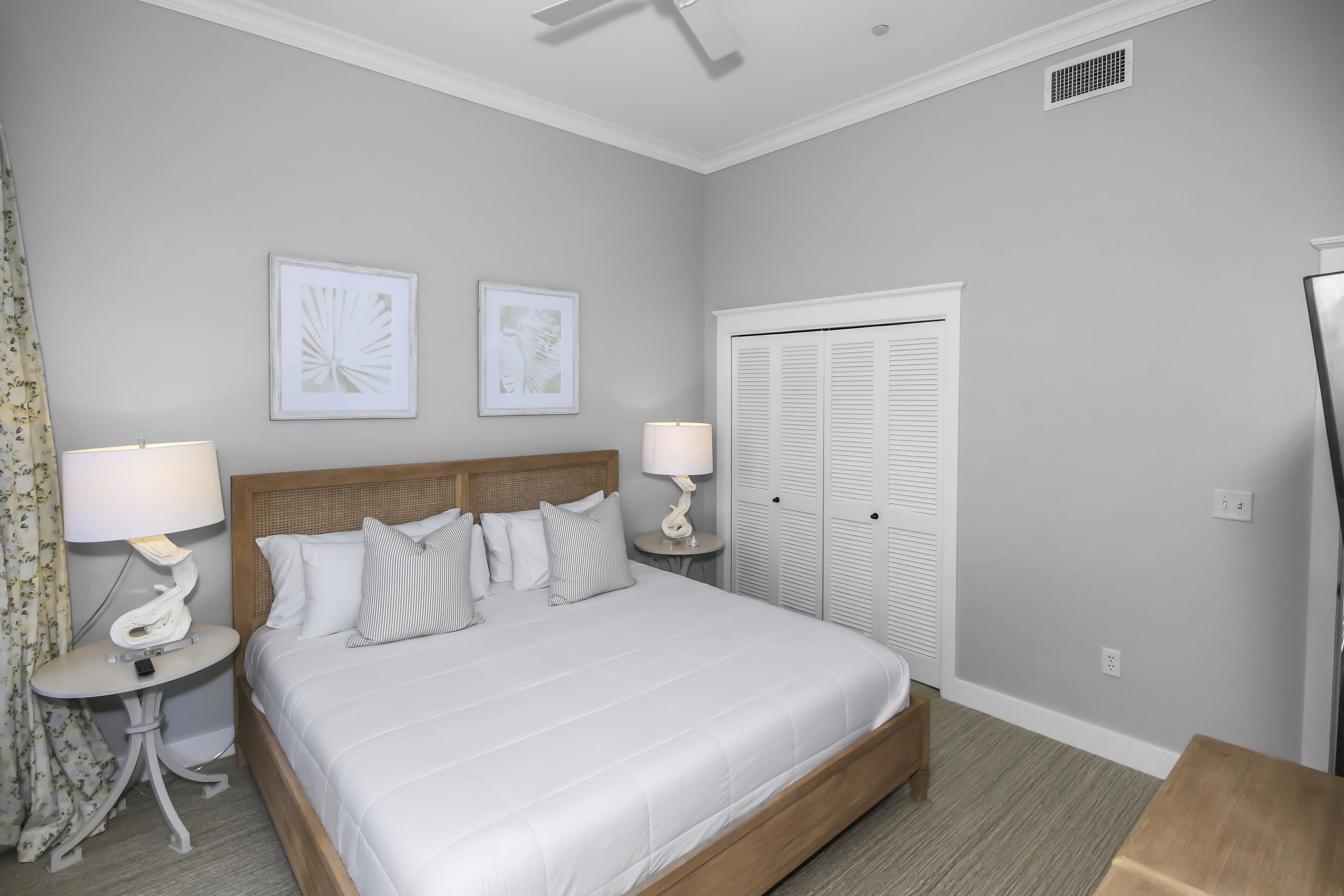 A neatly arranged bedroom with a large bed, two bedside tables with lamps, a wardrobe, and two framed pictures on the wall.
